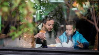 Father and son eating at a fast-food restaurant while looking at the food at a window seat