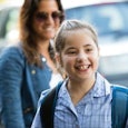 A smiling girl with special needs in a blue checked shirt and her mother in the back slightly blurre...