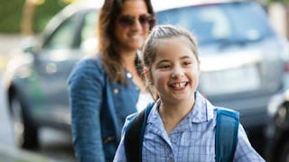 A smiling girl with special needs in a blue checked shirt and her mother in the back slightly blurre...