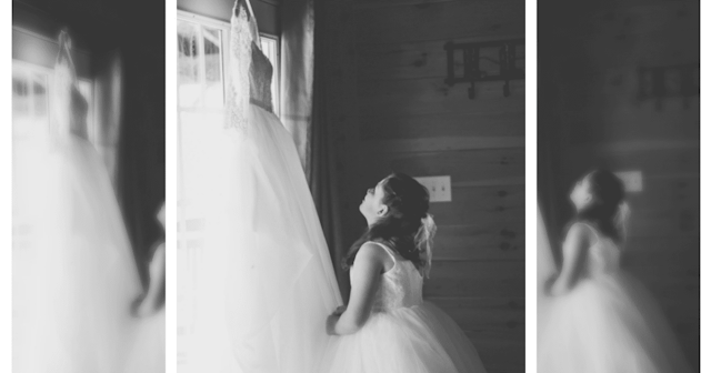 A black and white photo of a girl in a white dress looking up at a hanging wedding dress