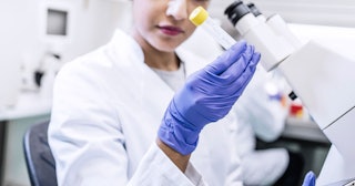 A woman in a laboratory looking at a test tube sitting at a desk with a microscope on it