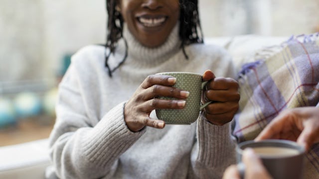 A woman smiling and sitting in winter clothes while holding a cup of coffee