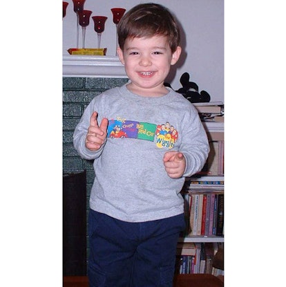 A little boy in a  grey sweater and dark blue denim jeans standing and smiling happily