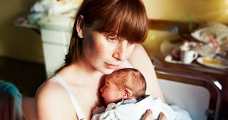 Tired postpartum mom holding her newborn in her arms.