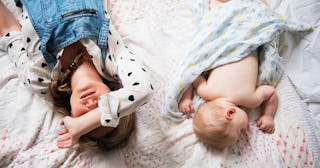 A young brown-haired girl lying on a bed next to her 2-year-old sibling