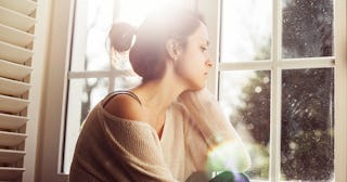 A motherless mother is sitting next to a window and looking through it in the distance