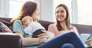 Two women wearing green and pink shirts while sitting on the couch and talking with the left woman h...