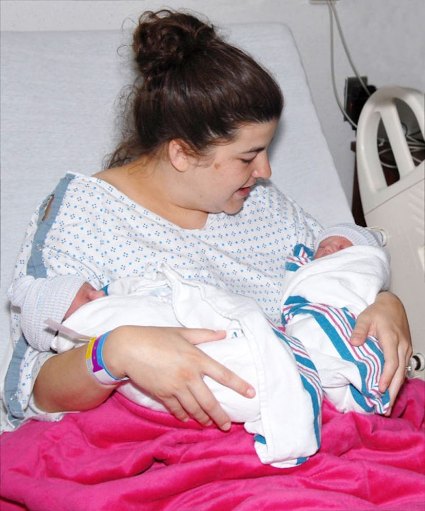 A surrogate on a hospital bed holding two babies in her hands that she birthed for another woman