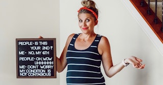 Pregnant woman with her 4th kid in striped shirt holding a funny sign about her pregnancy