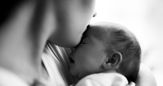 A young mother kissing her newborn baby on the head