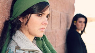 A girl estranged from her family leaning on a wall with a green scarf on her head, looking into the ...