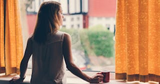 A young woman sadly looking outside through the window, while thinking about her miscarriages