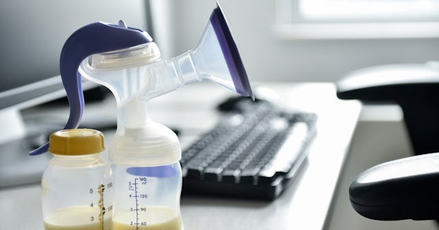 A breast pump and a bottle full of breast milk sitting on an office desk next to a monitor and a key...