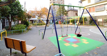 A playground in a park with swings, a slide and a bench