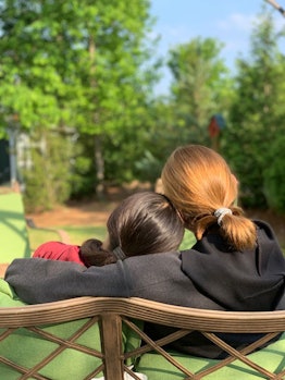 A red-haired girl hugging a brunette gril while sitting on a bench at a park