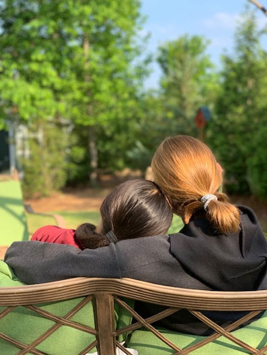 A red-haired girl hugging a brunette gril while sitting on a bench at a park