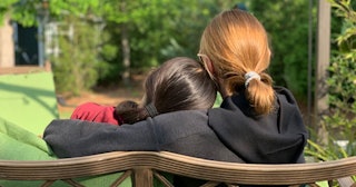 A girl hugging her friend while sitting on a bench at a park