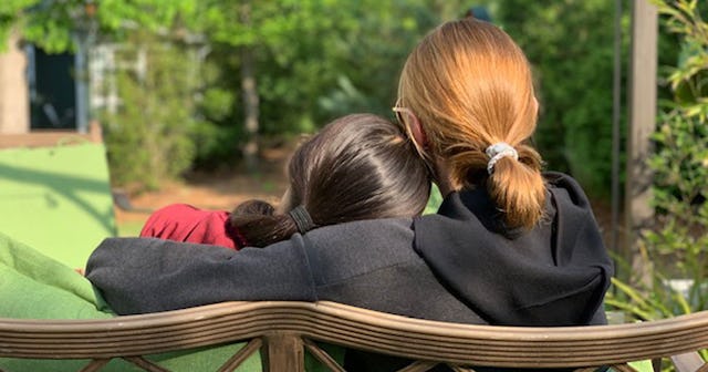A girl hugging her friend while sitting on a bench at a park