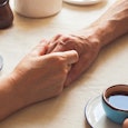 Husband and wife holding hands on the table and holding cups of coffee