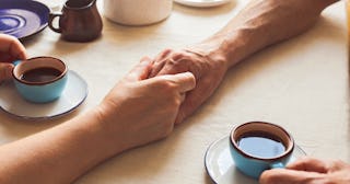 Husband and wife holding hands on the table and holding cups of coffee