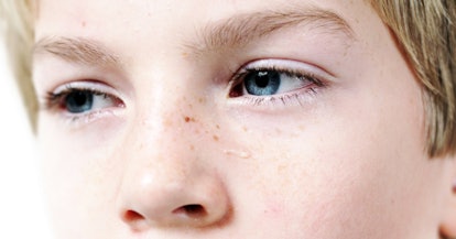 A blond  boy with blue eyes and freckles on the left side of his nose crying