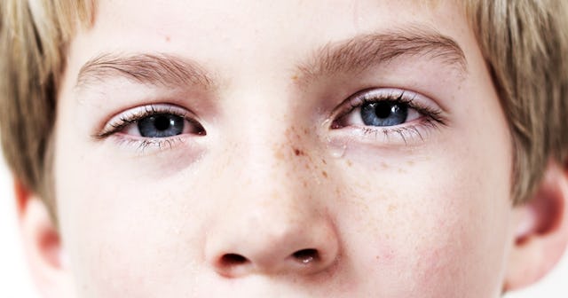 A blond, school-aged boy with blue eyes and freckles on the left side of his nose looking in front