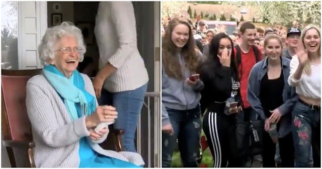 An elderly woman wearing blue and white clothes smiling while waving to students who are paying a mo...