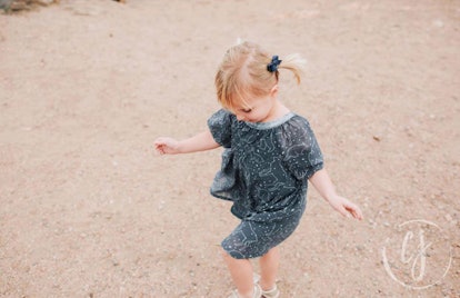 A little girl with bows in her hair and in a blue dress playing outside