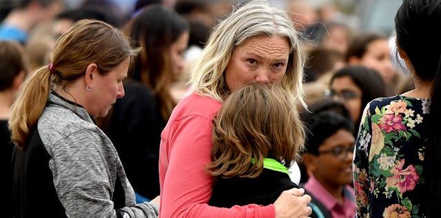 A mom holding and comforting her child in a group of people in the aftermath of a school shooting