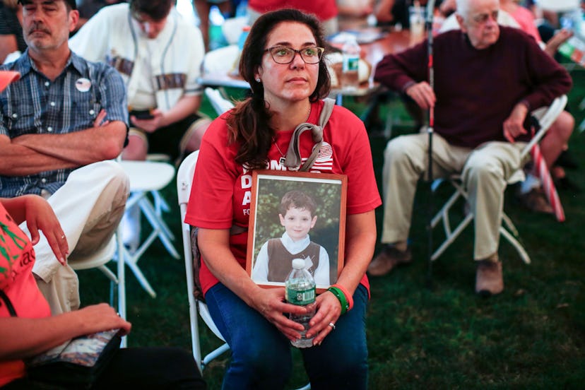 Brown haired woman sitting on a white chair holding a picture of her son that was a victim of school...