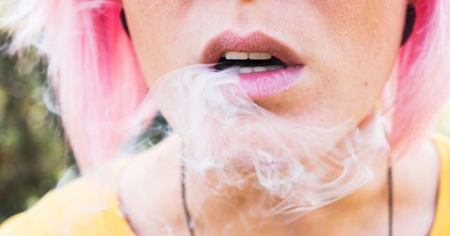 A close-up of a pink-haired woman's mouth, exhaling smoke.