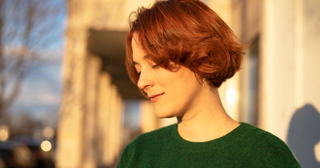 A young mother with brown hair of medium length is smiling while standing on the street who doesn't ...