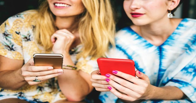 Two women smiling and scrolling through the Scary Mommy Baltimore Facebook Group on their phones