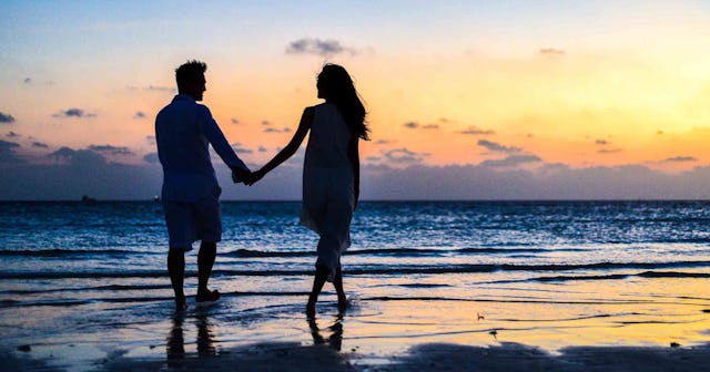 Married couple walking down on a beach holding hands while Sun is going down.