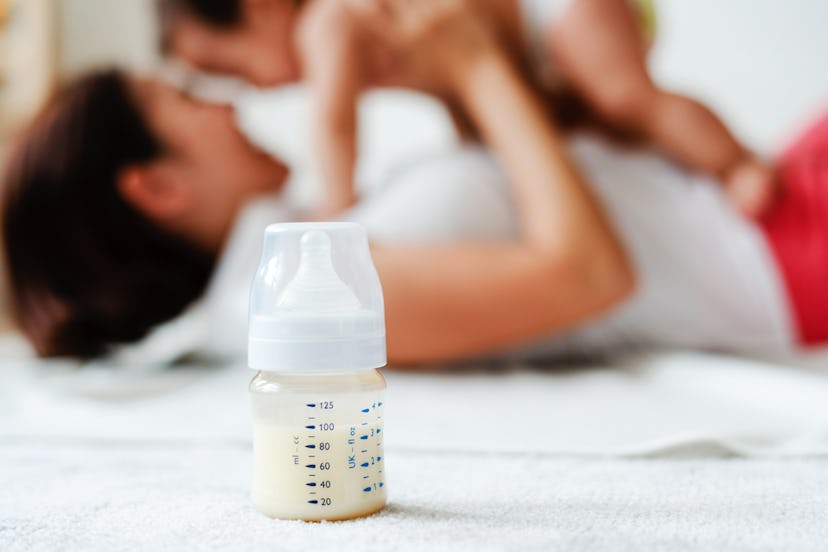 A blurred mother playing with her newborn baby on the floor with a milk bottle next to them