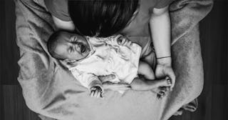 A mother holding her crying baby in her lap in black and white