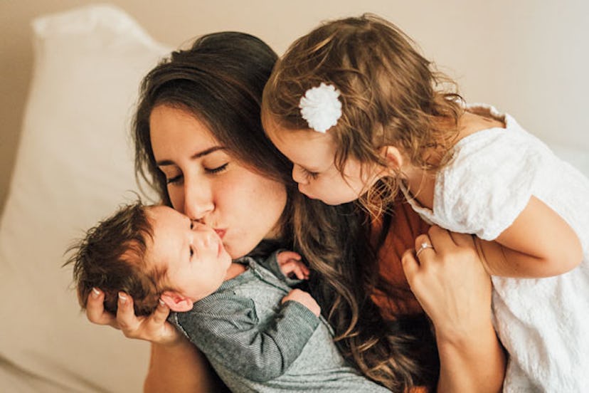 A mother kissing her baby and hugging her daughter 