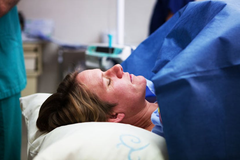 A dark blonde mother lying down while giving birth to her child