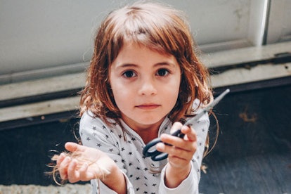 A little girl holding scissors in her hand after cutting her own hair 
