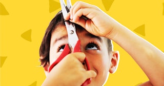 A boy cutting his own hair with red scissors in front of a yellow background