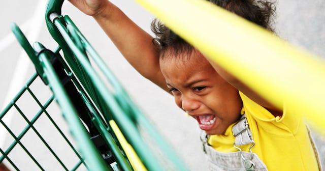 A little child attached to shopping cart while crying and screaming.