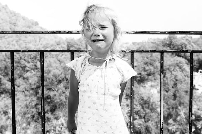 A little child in a floral dress crying with a fence behind her