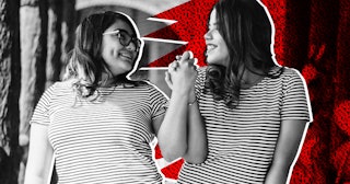 Two female friends in stripy t-shirts holding hands, looking at each other, and smiling.