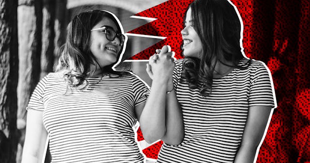 Two female friends in stripy t-shirts holding hands, looking at each other, and smiling.