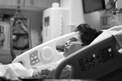 Black and white photo of a woman lying in a hospital bed with tubes in her nose