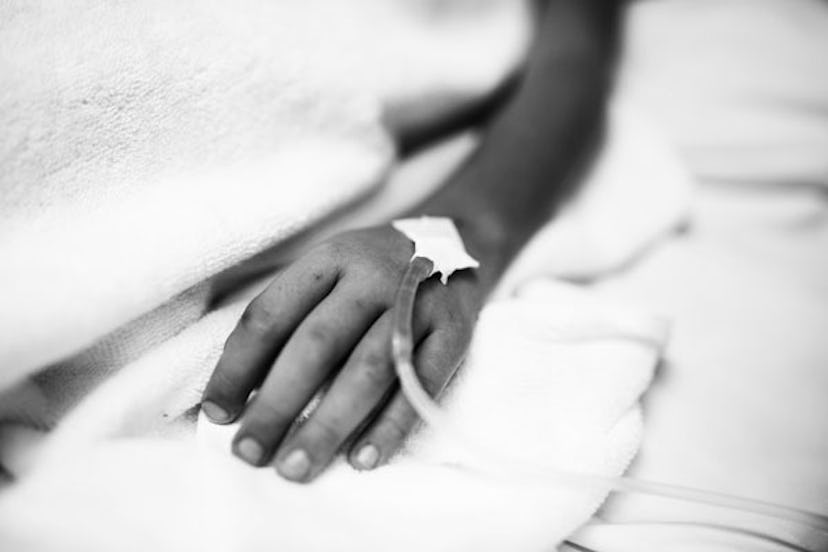 A Black and white photo of a hand on the bed with a transfusion tube inserted