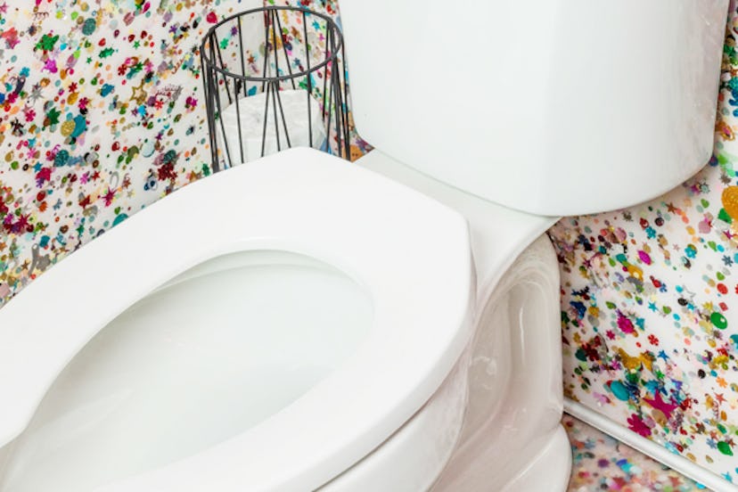 A close-up of a white toilet seat and the wall behind is dotted with various colors representing pos...