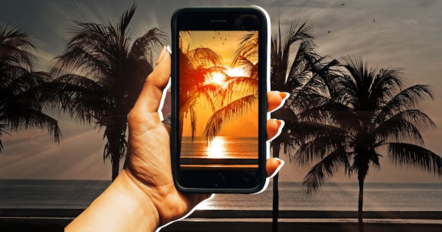 A person holding a phone and taking a picture of a sunset and palm trees with a filter on