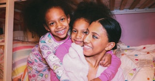 Two daughters cuddling with their mom, smiling.