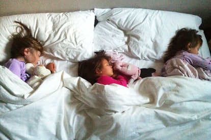 Three little girls sleeping in a bed together.